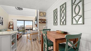Et moderne køkken med et træbord og grønne stole, en balkon med udsigt og dekorativ vægkunst.