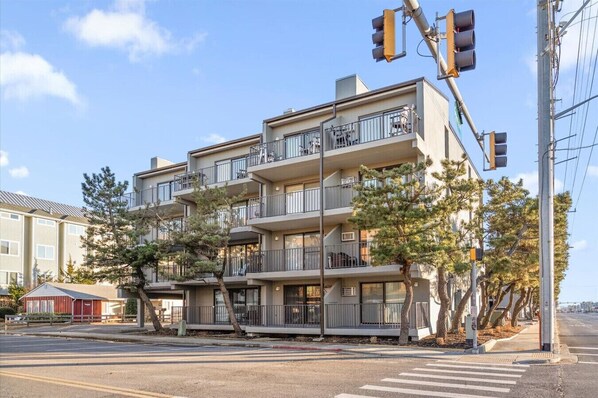 A multi-story residential building with balconies, a crosswalk, and street traffic lights.