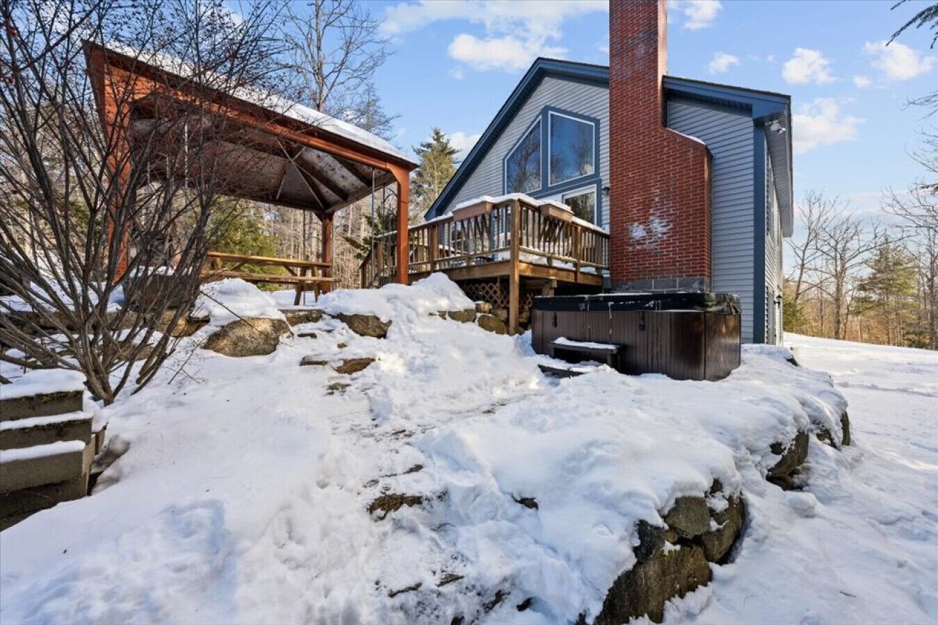 A modern house with a wooden deck, a brick chimney, and a snow-covered landscape.