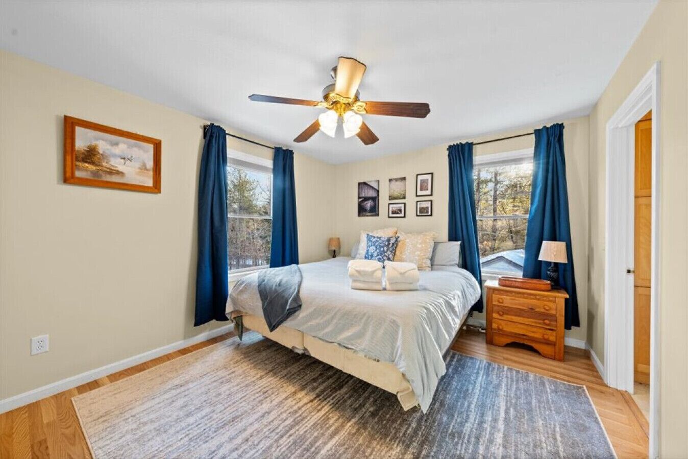 A bedroom with a bed, a ceiling fan, a nightstand, a lamp, and a window with curtains.