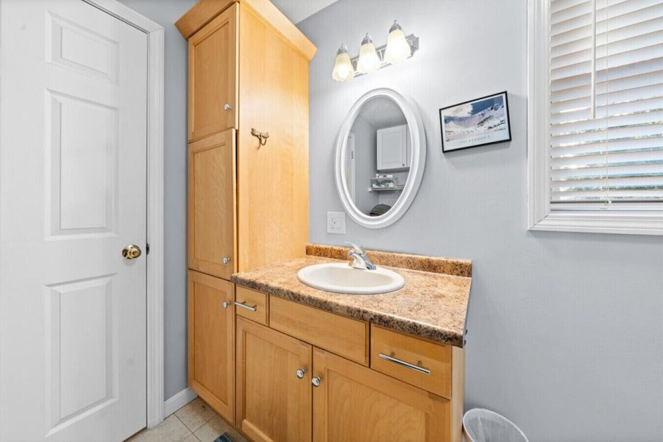 A bathroom with a wooden vanity, a white sink, and a mirror.