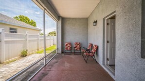 A covered patio with a concrete floor, a white fence, and a door leading to a garage. - Newer Construction Home in Port Richey, High Ceilings Screened Lanai & Lake View (Port Richey)