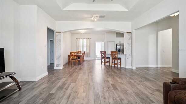 A spacious living area with a dining table and chairs, a ceiling fan, and a modern kitchen in the background. - Newer Construction Home in Port Richey, High Ceilings Screened Lanai & Lake View (Port Richey)