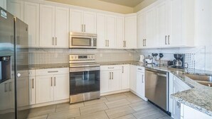 A modern kitchen with white cabinets, stainless steel appliances, and a tiled backsplash. - Newer Construction Home in Port Richey, High Ceilings Screened Lanai & Lake View (Port Richey)
