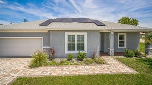 A single-story house with a garage, a small front yard with a brick pathway, and solar panels on the roof. - Newer Construction Home in Port Richey, High Ceilings Screened Lanai & Lake View (Port Richey)