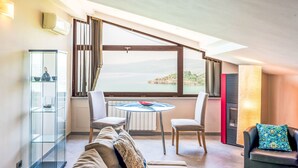 A modern living room with a glass table, two chairs, a sofa, and a view of a lake.