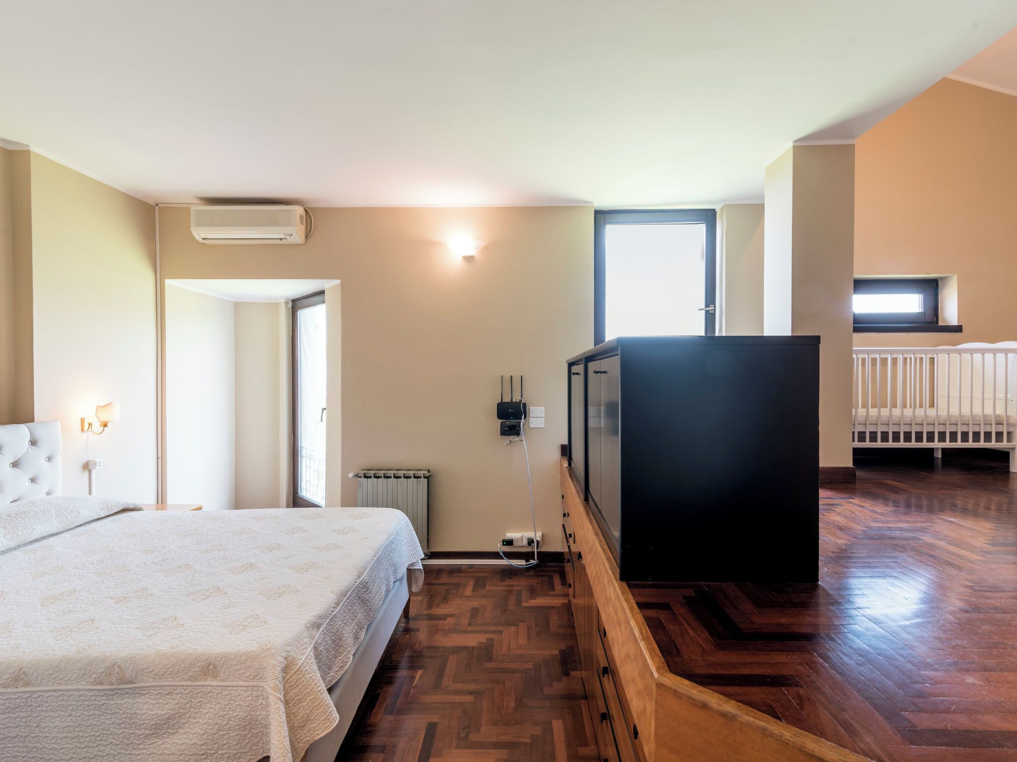 A bedroom with a bed, a TV, a radiator, and a crib in the adjacent room.