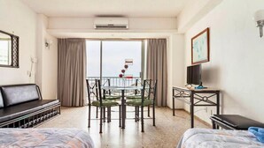 A hotel room with two beds, a dining table with chairs, a TV, and a balcony with a view. - Suite 1808 by Suites Victoria Acapulco (Acapulco de Juárez)