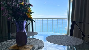 A balcony with a glass table and chairs, a purple vase with flowers, and a view of the ocean. - Suite 1808 by Suites Victoria Acapulco (Acapulco de Juárez)