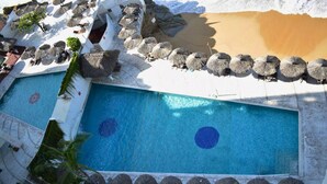 A pool area with multiple sun loungers and umbrellas, surrounded by a stone wall and a beach. - Suite 1808 by Suites Victoria Acapulco (Acapulco de Juárez)