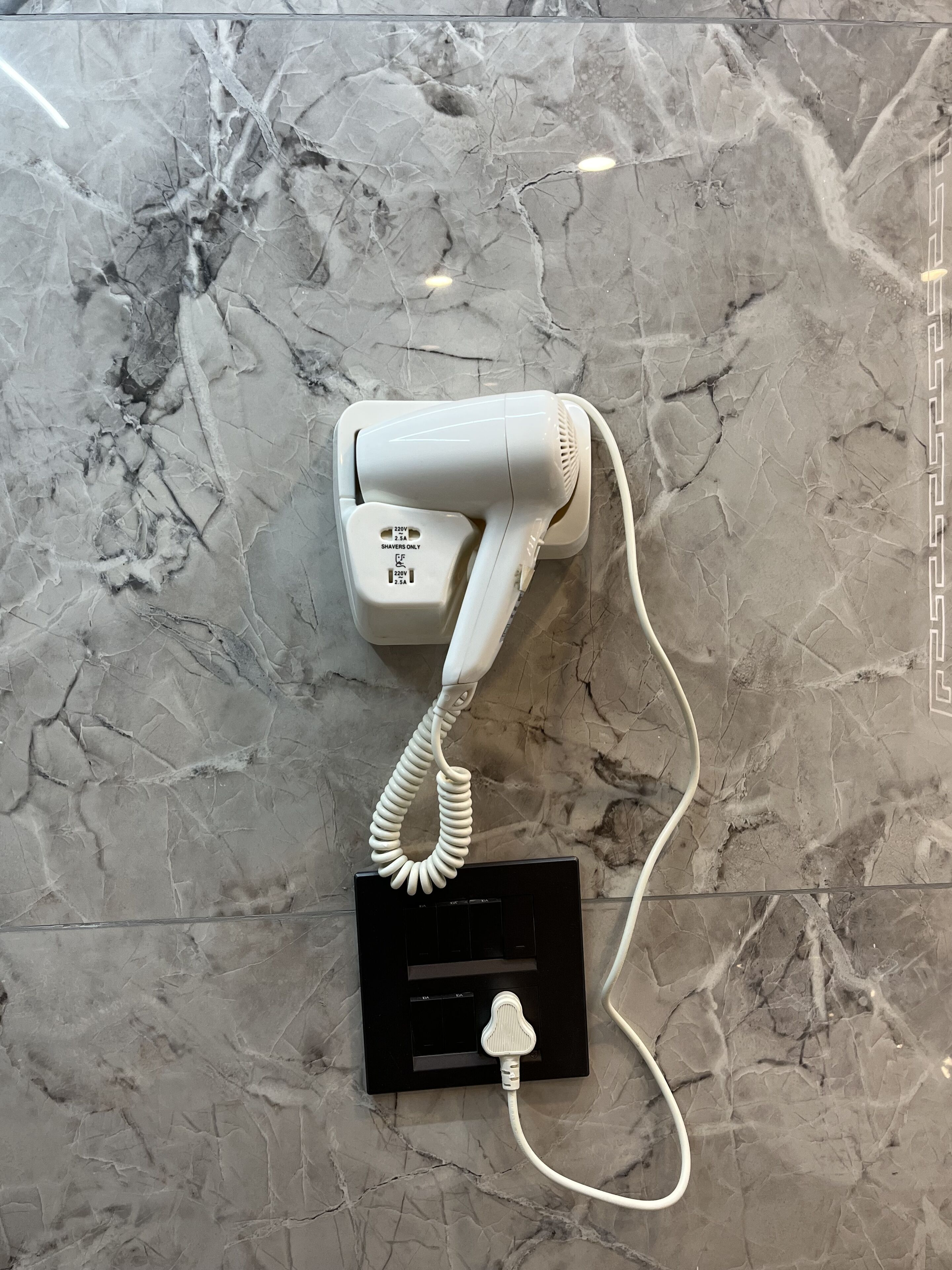 A hair dryer mounted on a marble wall with a power strip below.