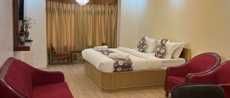 A modern bedroom with a bed, two red armchairs, a black office chair, a wooden desk, and a wooden floor.