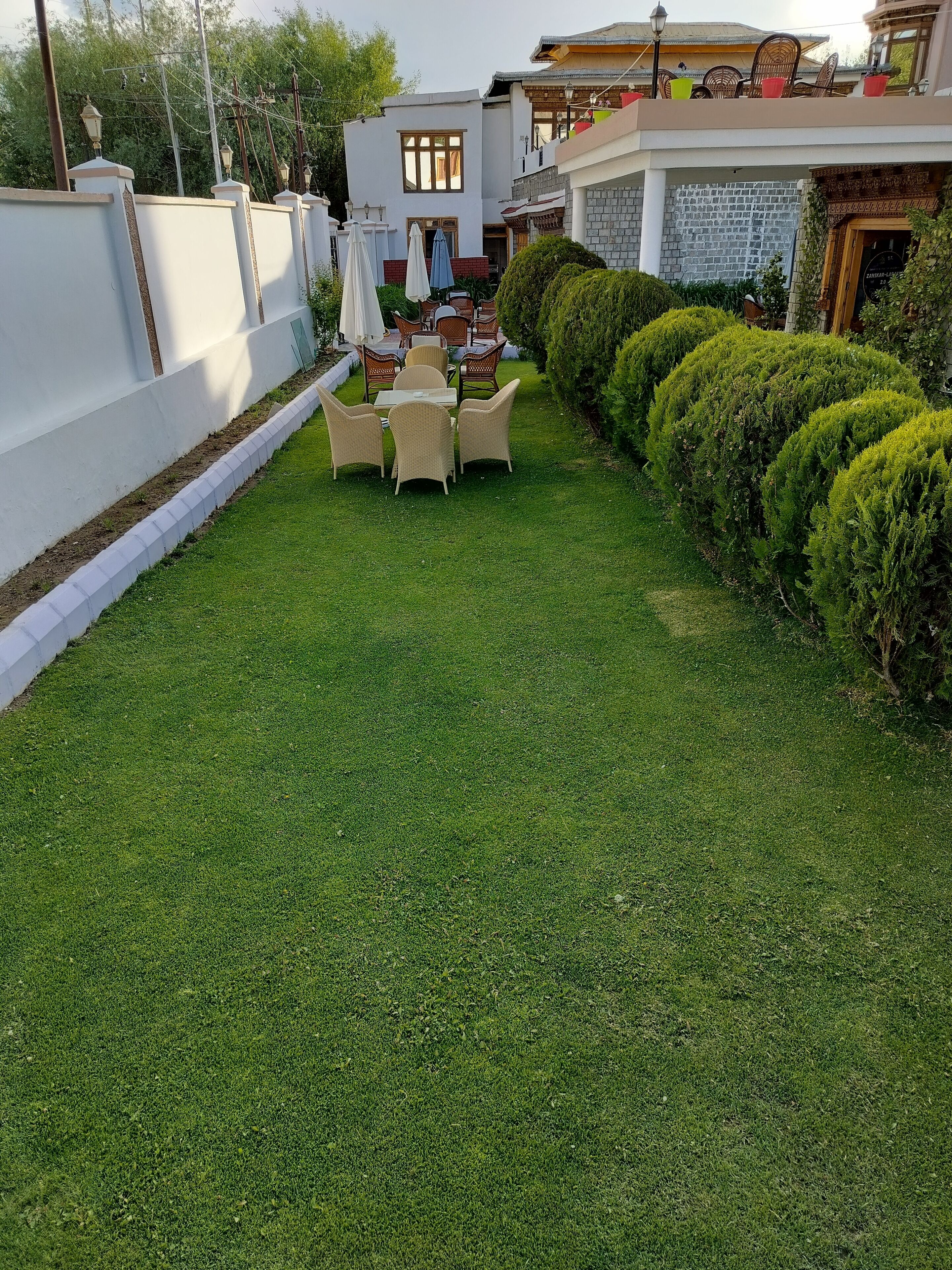 A well-maintained lawn with a dining area featuring wicker furniture and umbrellas.