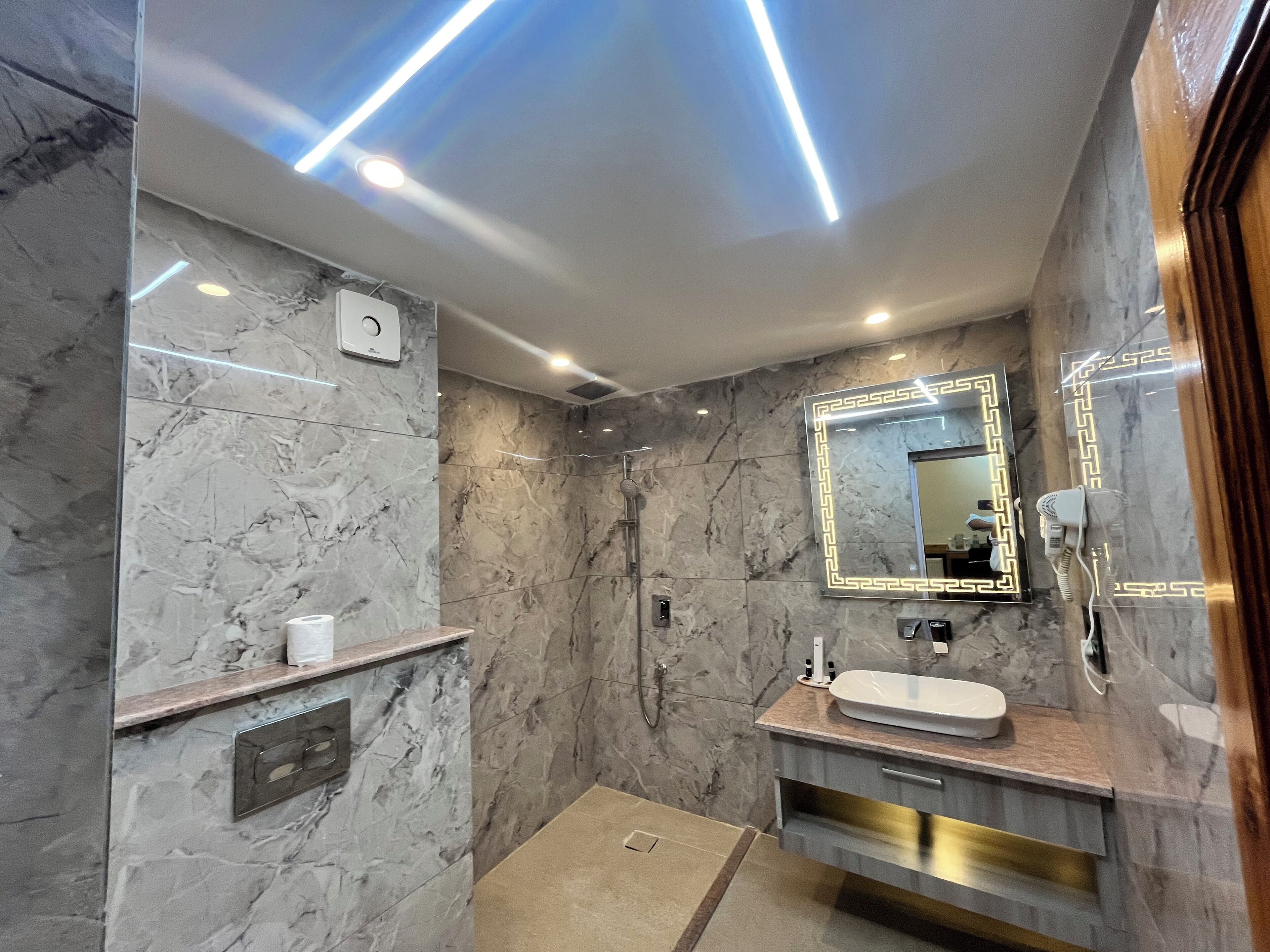 A modern bathroom with marble walls, a vanity with a sink, a mirror with LED lighting, and a shower area.