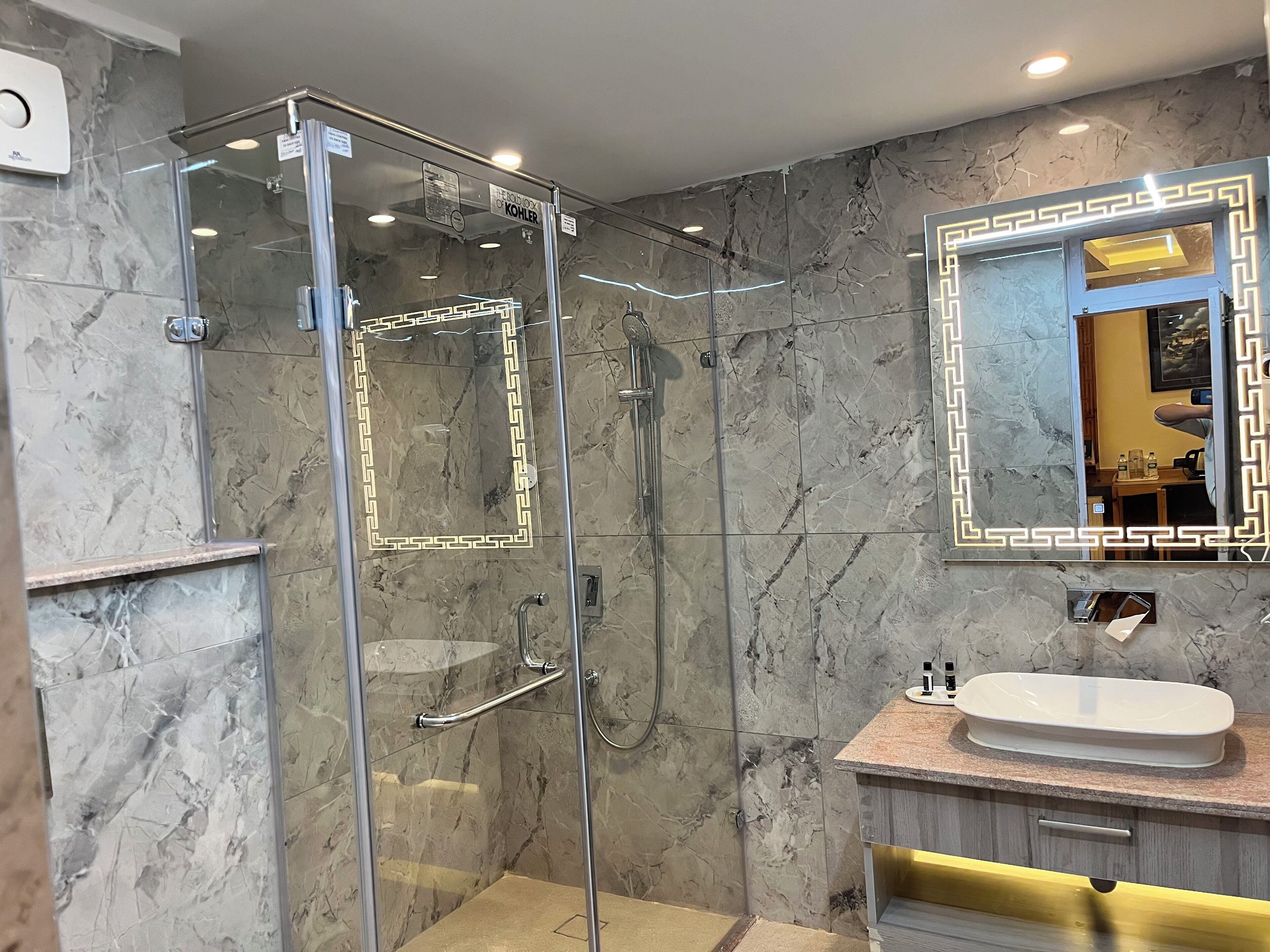 Een moderne badkamer met een douchecabine van glas, marmeren wanden en een wastafel met een wastafel en spiegel.
