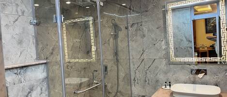 A modern bathroom with a glass-enclosed shower, marble walls, and a vanity with a sink and mirror.