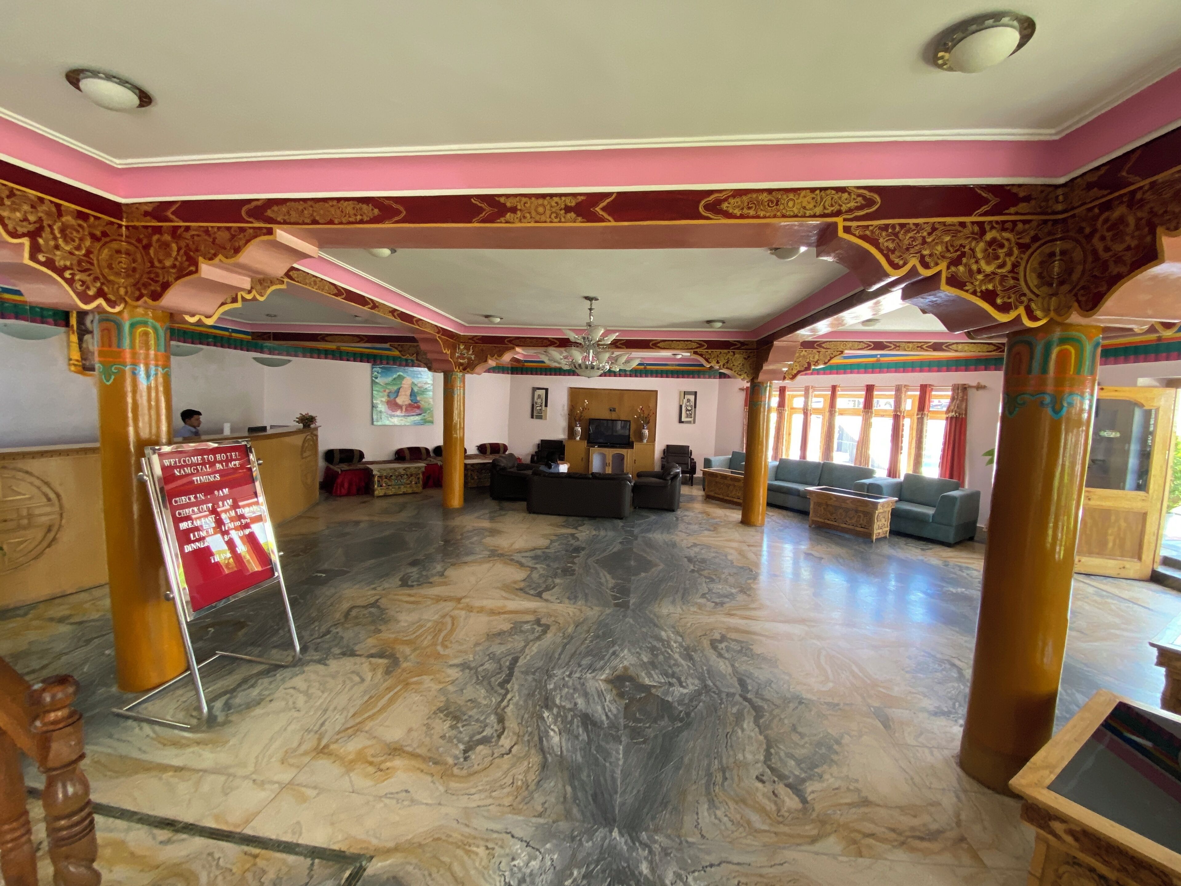 A hotel lobby with a marble floor, a reception desk, and a seating area with sofas and chairs.