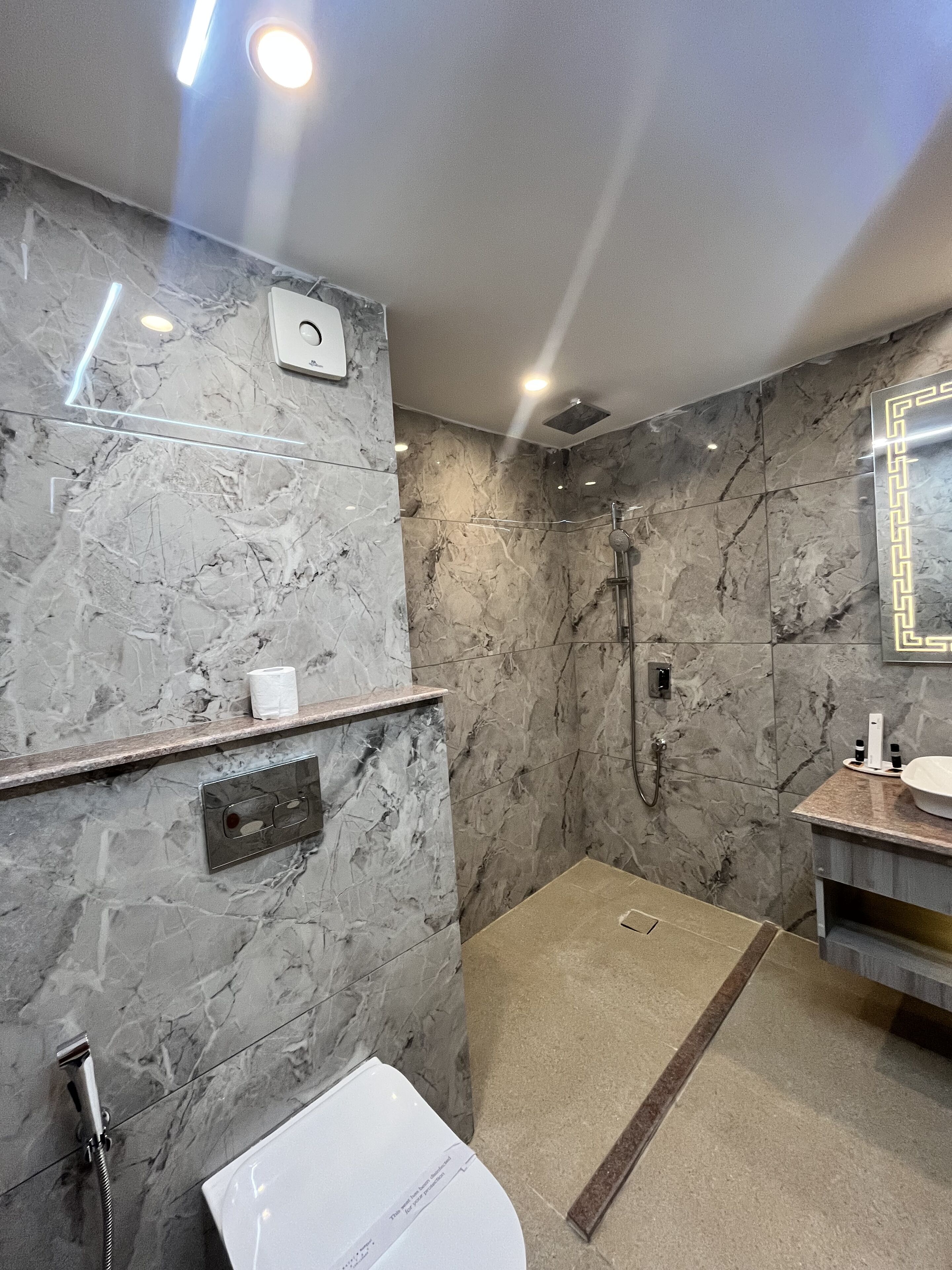 Ein modernes Badezimmer mit Marmorwand, Dusche, Toilette und Waschtisch mit Spiegel.