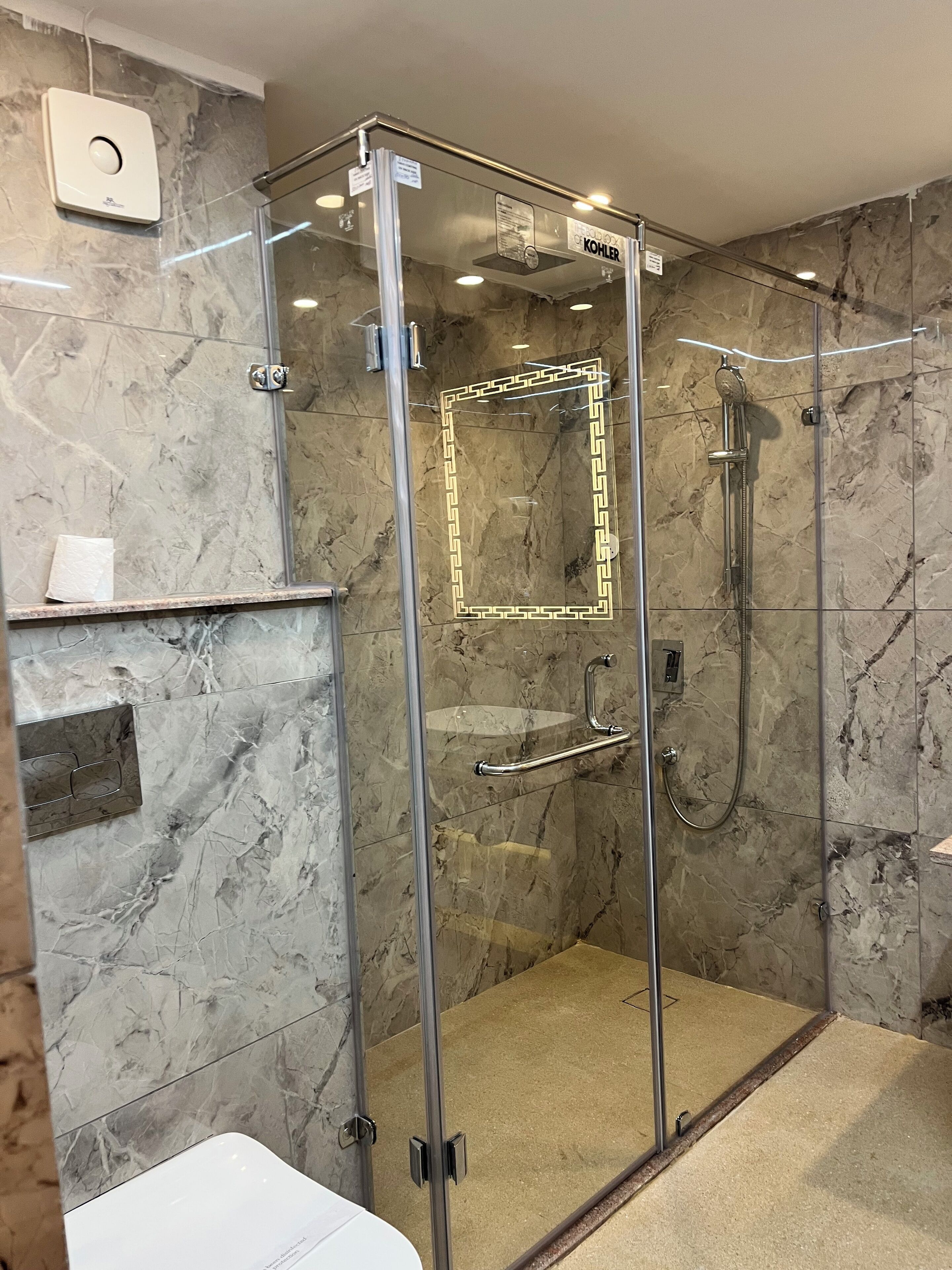 Ducha con cerramiento de vidrio, pared de mármol, dispensador de toallas y ducha Kohler.