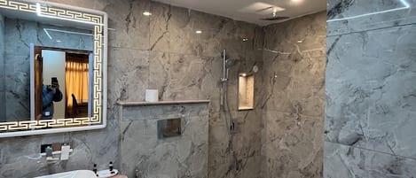 Een moderne badkamer met een marmeren wand, een grote spiegel, een wastafel en een douche.