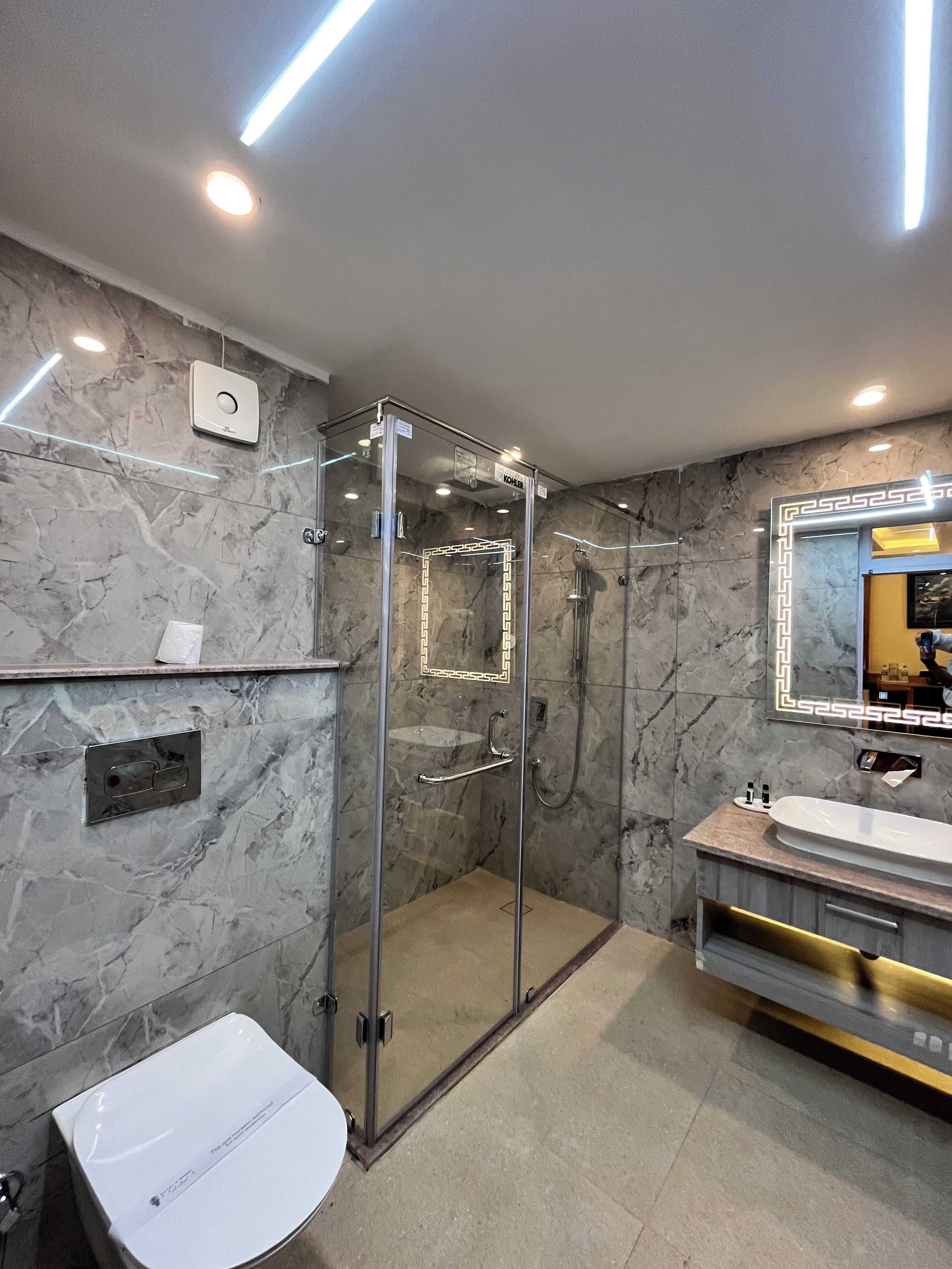 A modern bathroom with a glass-enclosed shower, a white sink, and a marble wall.