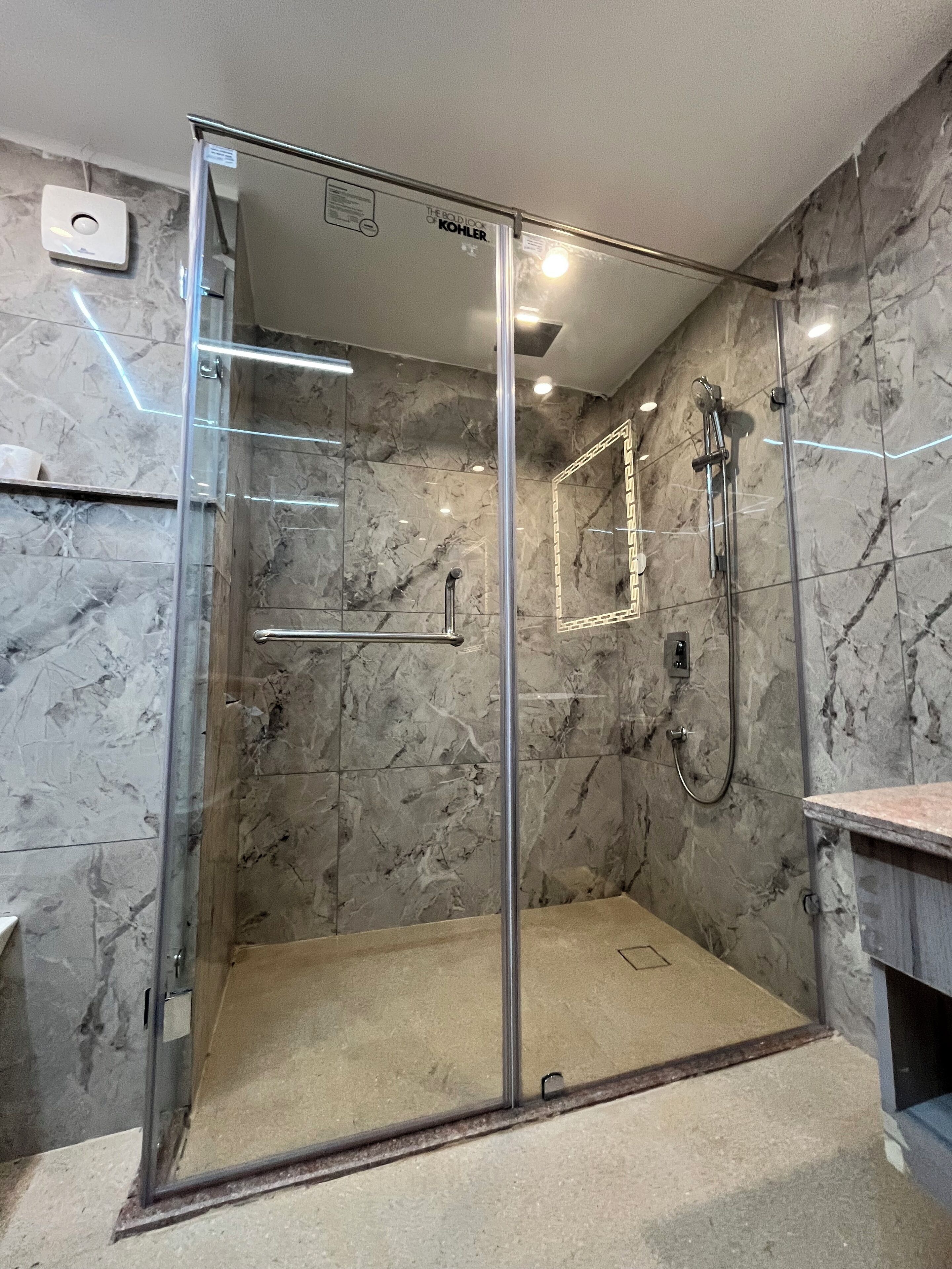 A glass-enclosed shower with a marble wall, a handheld showerhead, and a handheld shower head.