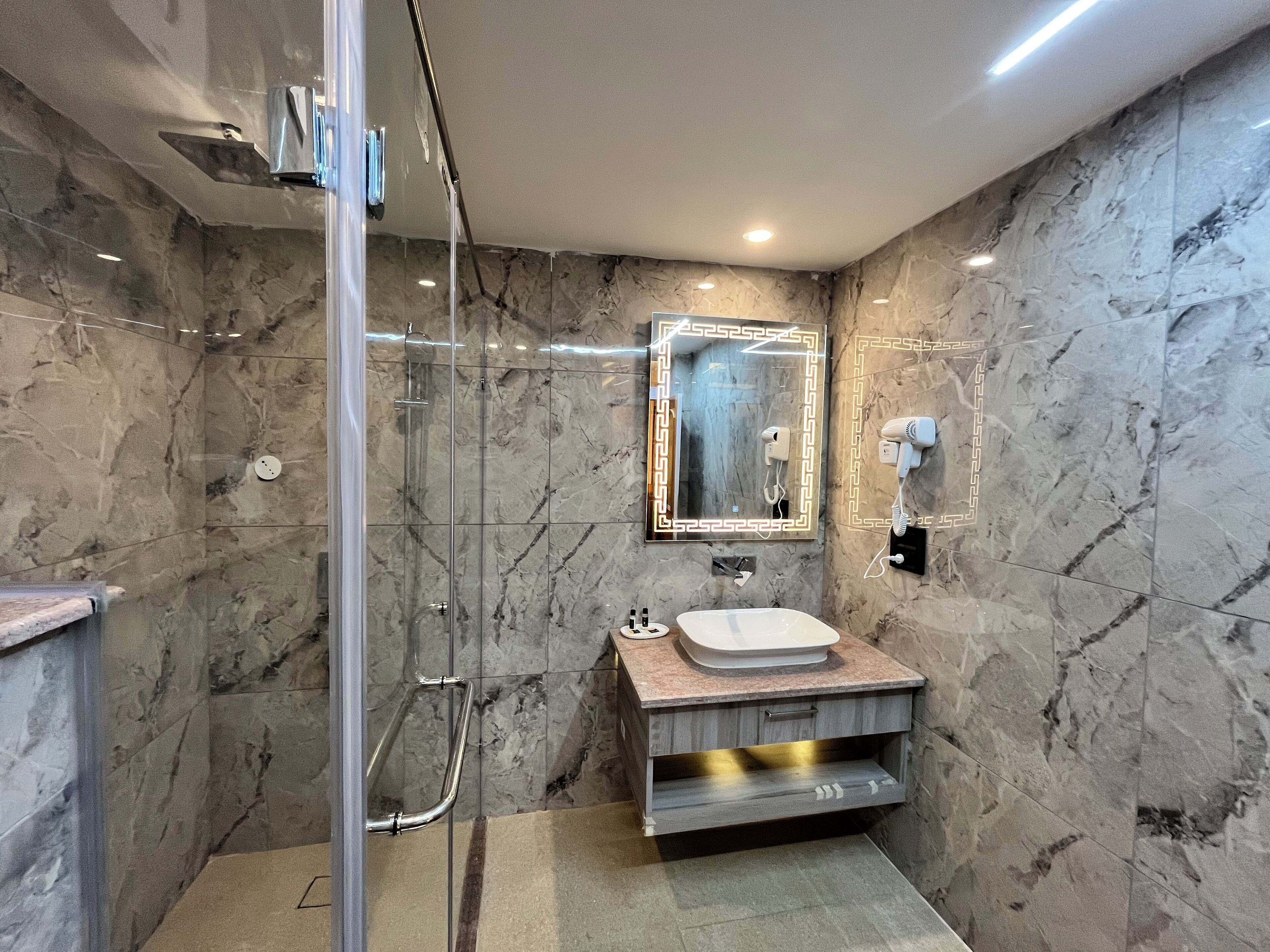 A modern bathroom with a glass-enclosed shower, a marble wall, a vanity with a sink, and a hairdryer mounted on the wall.
