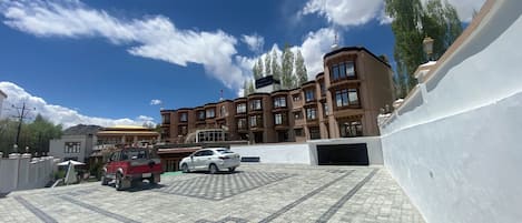 A hotel with a modern architectural design, featuring a large building with multiple windows and balconies. There is a parking area with several cars and a red vehicle.