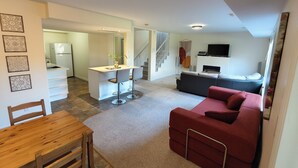 Amplia sala de estar con cocina, una mesa de comedor con sillas, un sofá rojo y un televisor montado en la pared.
