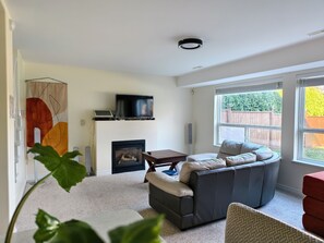 Una sala de estar con chimenea, un sofá, un televisor y un ventanal grande.