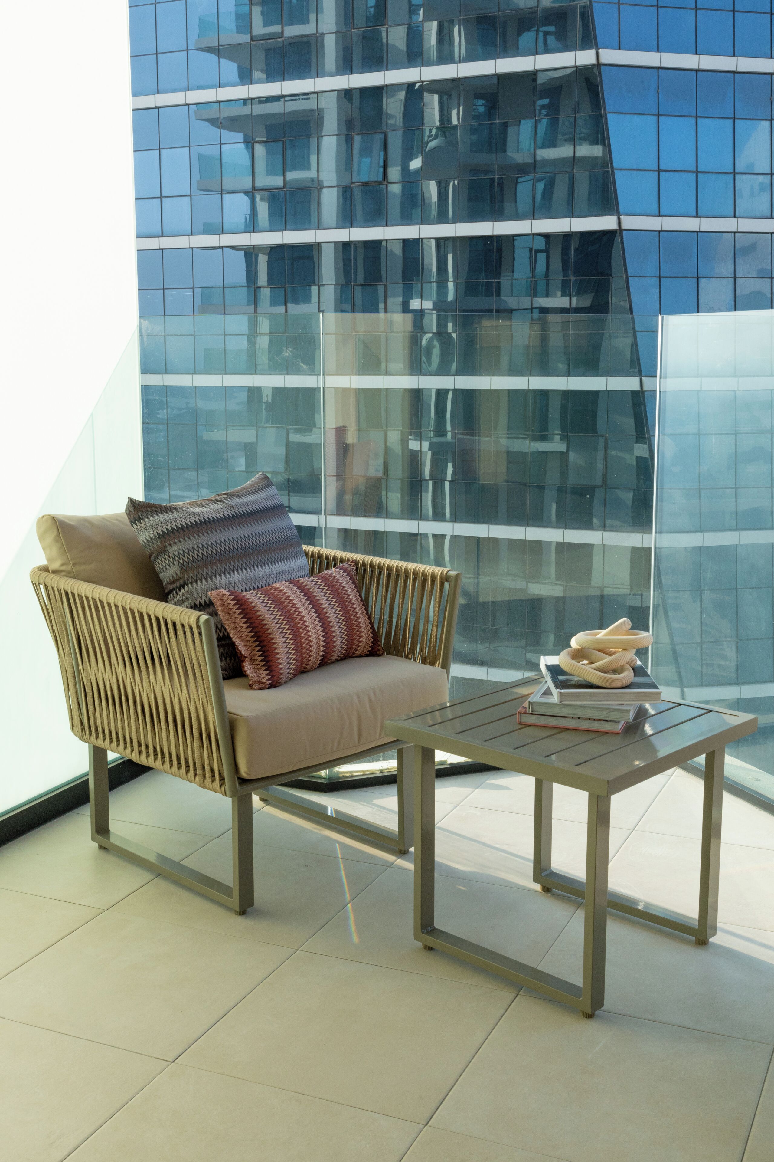 A modern lounge area with a wicker chair, a glass table, and a view of a glass building.