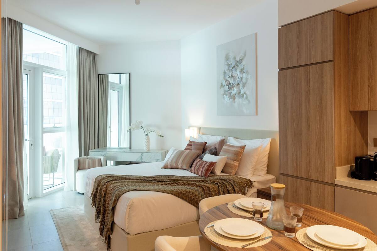 Ett modernt hotellrum med en stor säng, ett matbord för två personer, en sittgrupp med en soffa och utsikt över staden genom fönstret.