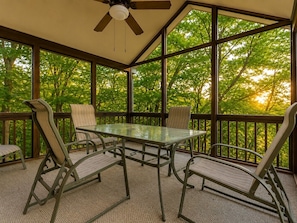 A covered patio with a glass table and metal chairs, surrounded by large windows.