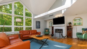 A spacious living room with a fireplace, leather sofas, and a large window overlooking greenery. - 3 bedroom 3 bath, expansive views Treehouse feel (Galena)