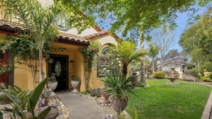 A house with a tiled roof, a stone pathway leading to the entrance, and a well-maintained garden with various plants and a birdbath. - Acanto Del Mar (Aptos)