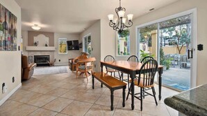 A spacious living room with a fireplace, a dining area with a wooden table and chairs, and a large sliding glass door leading to a patio. - Acanto Del Mar (Aptos)