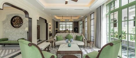 A spacious living room with a sofa, two green armchairs, a coffee table, and a ceiling fan.