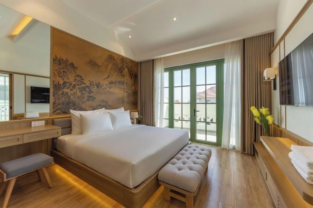 Une chambre d’hôtel avec un grand lit, un bureau, une banquette, une télévision et une vue sur l’extérieur, visible à travers une porte verte.