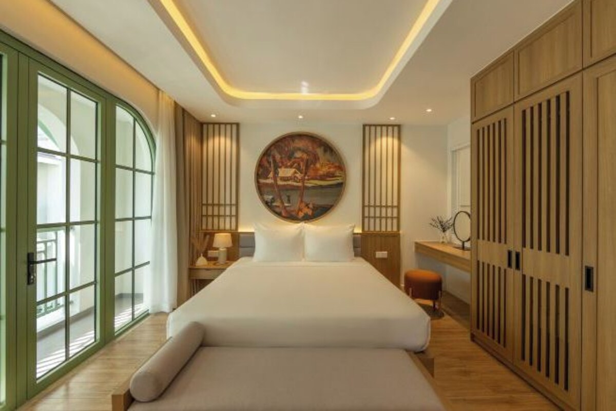 Une chambre d’hôtel moderne avec un grand lit, un tableau au mur et une armoire en bois.
