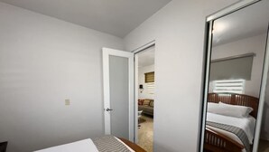 A bedroom with a bed, a mirror, and a door leading to another room. - Casa Luquillo | Cozy Retreat House W/ BBQs & Tub (Luquillo)