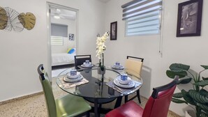 A compact dining area with a round glass table set for four, surrounded by chairs with cushioned seats. - Casa Luquillo | Cozy Retreat House W/ BBQs & Tub (Luquillo)