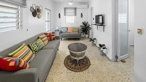 A modern living room with a grey sofa, colorful cushions, a round coffee table, and a small plant. - Casa Luquillo | Cozy Retreat House W/ BBQs & Tub (Luquillo)