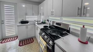 A modern kitchen with white cabinets, a stove, and a window with blinds. - Casa Luquillo | Cozy Retreat House W/ BBQs & Tub (Luquillo)