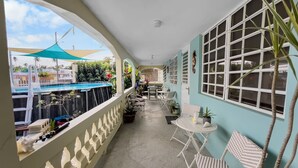 Ein überdachter Balkon mit Blick auf einen Pool, einem Tisch mit Stühlen und Blumentöpfen.