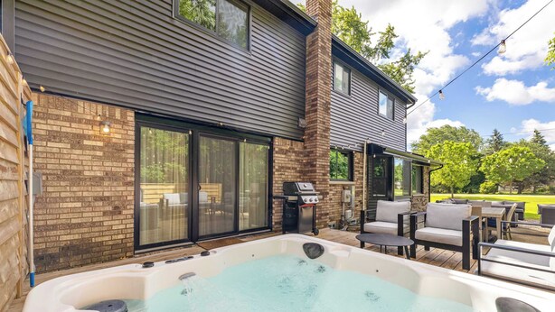 A hot tub with a brick wall and sliding glass doors, outdoor furniture, and a barbecue grill. - Newly Renovated 5BR/2.5BA w/ Jacuzzi! (Rochester Hills)