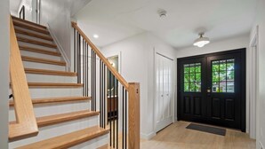 A staircase with wooden steps and black railings, a black door with glass panels, and a light-colored floor. - Newly Renovated 5BR/2.5BA w/ Jacuzzi! (Rochester Hills)