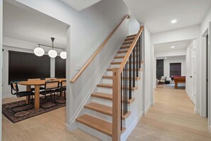 A modern interior with a wooden staircase, a dining area with a table and chairs, and a pool table in the background.