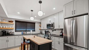 A modern kitchen with a central island, stainless steel appliances, and wooden accents. - Newly Renovated 5BR/2.5BA w/ Jacuzzi! (Rochester Hills)