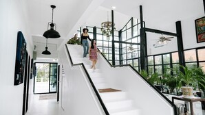 Una escalera con paredes blancas y barandillas negras que conduce a una plataforma con ventanas grandes y plantas en macetas.