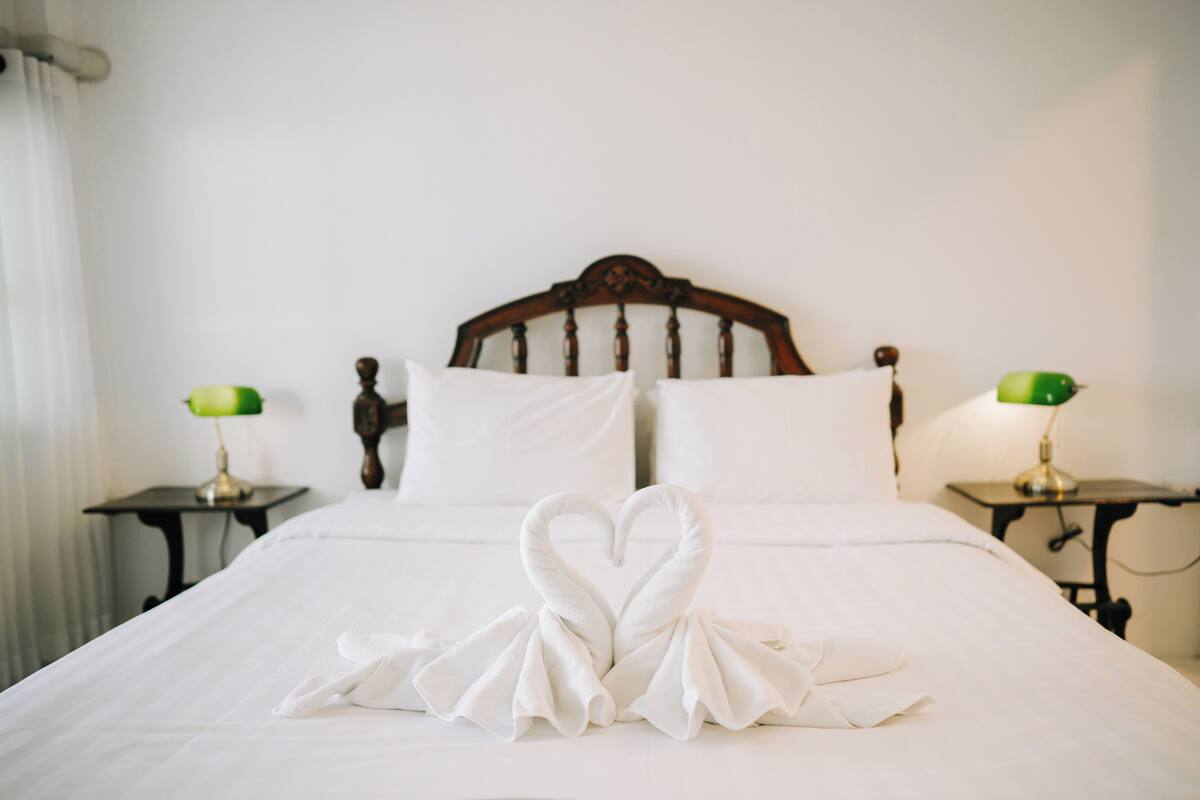 A neatly made bed with white linens and two green lamps on side tables.